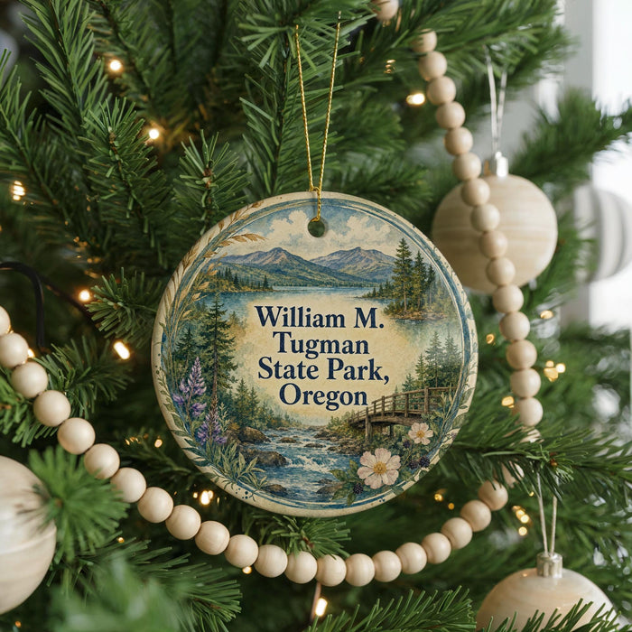 A round ornament hanging on a Christmas tree, featuring a scenic landscape with mountains, a river, and a bridge.