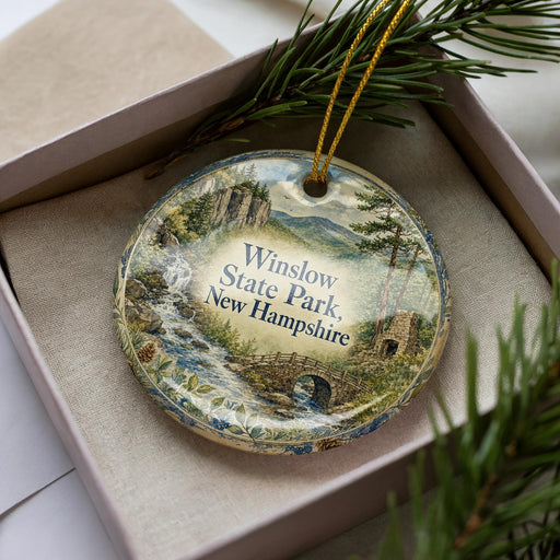 A decorative ornament with a scenic landscape of Winslow State Park in New Hampshire, featuring a bridge, trees, and a waterfall.