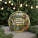 A decorative ornament featuring a scenic landscape with a waterfall, pine trees, and a bridge, hanging from a string.