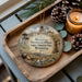 A decorative ornament featuring a scene from the Territorial Prison State Historic Site in Wyoming, with a candle and pine cones on a wooden tray.