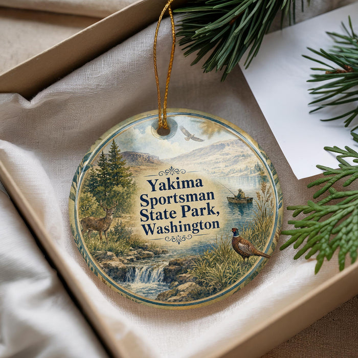 A decorative ornament with a scenic landscape featuring a waterfall, pine trees, and wildlife, including a deer and a bird, is displayed in a box.