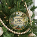 A round ornament hanging on a Christmas tree, featuring a scenic landscape with a lake, a dock, and a bird.