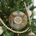A round ornament hanging on a Christmas tree, featuring a scenic landscape with a waterfall and mountains.