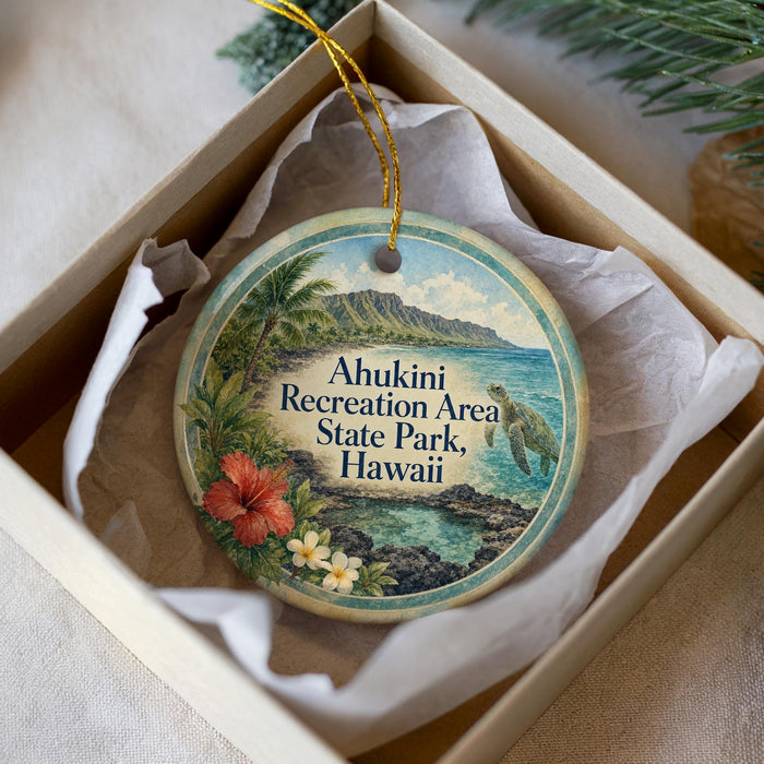 A round ornament with a tropical beach scene and a sea turtle, placed in a white box with a gold string.