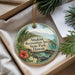 A round ornament with a tropical beach scene and text, placed in a box with pine branches.