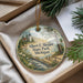 A decorative ornament with a lighthouse and a scenic landscape, placed in a box with pine branches.