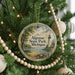 A round ornament hanging on a Christmas tree, featuring a lighthouse and a scenic landscape.