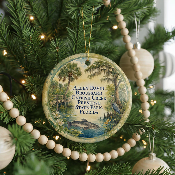 A round ornament hanging on a Christmas tree, featuring a scenic image of a pond with a bird and palm trees.