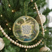 A round ornament hanging on a Christmas tree, featuring a scenic image of a pond with a bird and palm trees.