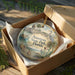 A decorative ornament in a box, featuring a scenic landscape with palm trees, a bird, and other natural elements, along with the text "Anastasia State Park, Florida".