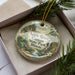 A decorative ornament in a box, featuring a scenic landscape of the Apple River Canyon State Park in Illinois.