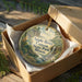 A decorative ornament in a brown box, featuring a scenic landscape of the Apple River Canyon State Park in Illinois.