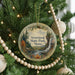 A round ornament hanging on a Christmas tree, featuring a scenic landscape with a waterfall and pine trees.