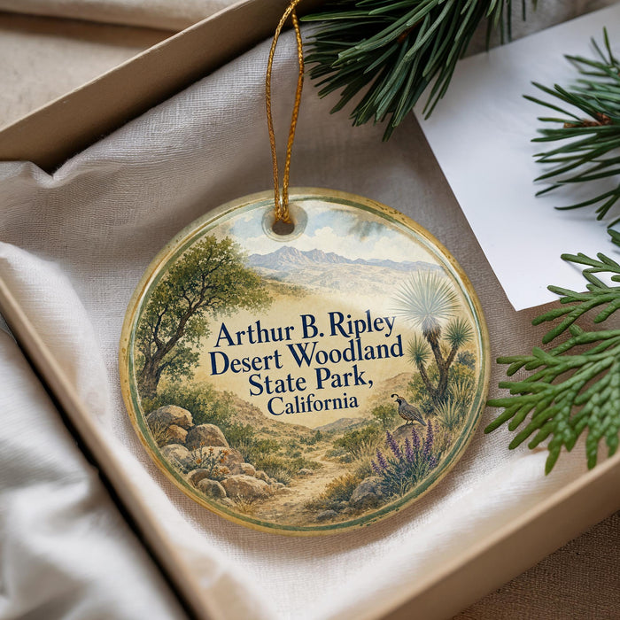 A decorative ornament with a landscape scene featuring mountains, trees, and a bird, placed in a box with pine branches.