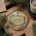 A decorative ornament with a landscape scene featuring mountains, trees, and a winding path, hanging on a wooden surface.