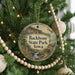 A round ornament hanging on a Christmas tree, featuring a scenic landscape with a river and a house.