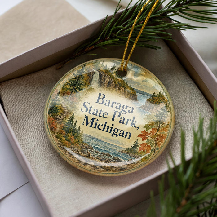 A decorative ornament in a box, featuring a scenic landscape with a lake, mountains, and pine trees.