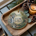 A wooden tray with a decorative ornament featuring a scenic image of a waterfall and forest, accompanied by pine cones and a lit candle.