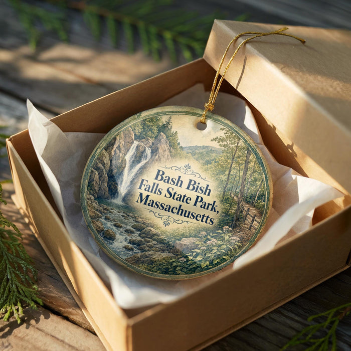 A round ornament in a box, featuring a scenic image of a waterfall surrounded by trees and greenery, with the text "Bash Bish Falls State Park Massachusetts" printed on it.