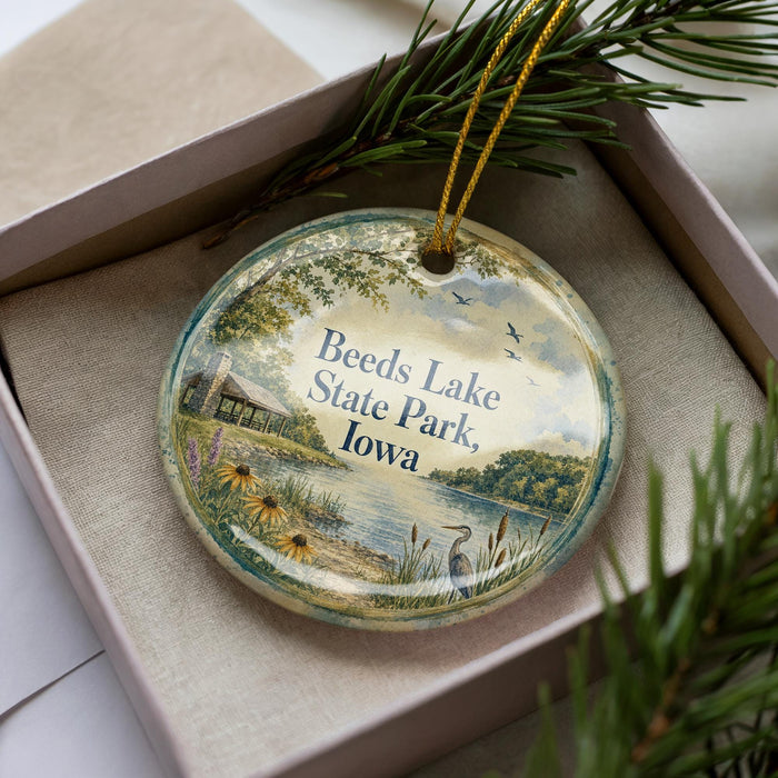 A decorative ornament in a box, featuring a scenic landscape with a lake, trees, and birds.
