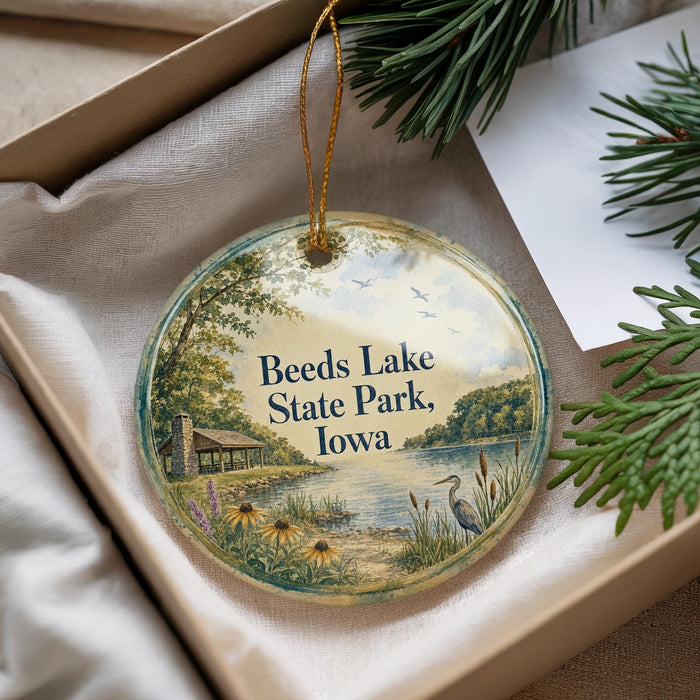 A decorative ornament with a scenic lake and park scene, featuring a bird and greenery, is displayed in a box.
