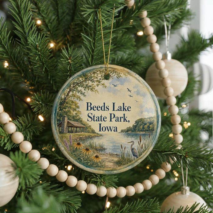 A round ornament hanging on a Christmas tree, featuring a scenic landscape with a lake, trees, and birds.