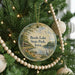 A round ornament hanging on a Christmas tree, featuring a scenic landscape with a lake, trees, and birds.