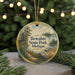 A round ornament with a painting of a scenic landscape, featuring a lake, pine trees, and a cabin, hanging from a string.