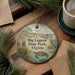 A circular ornament with a painting of a bird, a turtle, and a boat on a lake, surrounded by pine branches and a cup of coffee on a wooden surface.