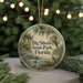 A round ornament with a painting of Big Shoals State Park, Florida, featuring a bird and a river, is displayed on a table with a blurred background of a Christmas tree.
