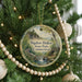 A round ornament hanging on a Christmas tree, featuring a scenic landscape with a waterfall and a bridge.