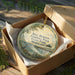 A round ornament in a box, featuring a scenic image of a pier and a bird, with the text "Bill Burton Fishing Pier State Park, Maryland" printed on it.