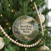 A round ornament hanging on a Christmas tree, featuring a scenic landscape with a path leading to a lake, surrounded by pine trees and a clear sky.