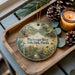 A decorative ornament featuring a scenic view of the Blackwater River State Park in Florida, with a bird perched on a palm tree and a wooden bridge in the background.