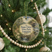A round ornament hanging on a Christmas tree, featuring a scenic image of a bridge and a river surrounded by trees and greenery.