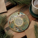 A decorative ornament featuring a scenic landscape with mountains, cacti, and a stream, hanging on a wooden surface.