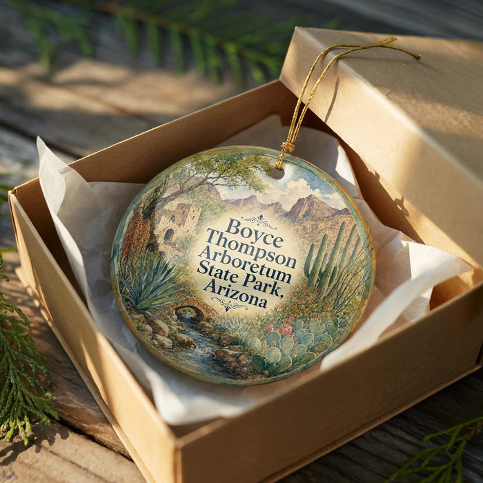 A decorative ornament in a brown box, featuring a scenic landscape with mountains, cacti, and a stream.
