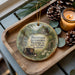A wooden tray with a decorative ornament featuring a scenic image of Ironworks Historical State Park, Alabama, and pine cones.