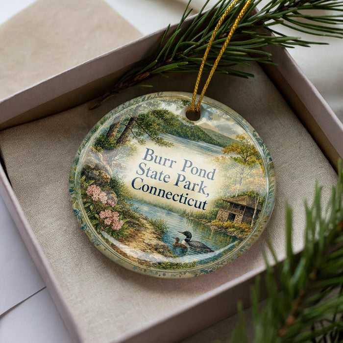 A decorative ornament with a scenic landscape of Burn Pond State Park in Connecticut, featuring a lake, trees, and a cabin.