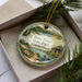A decorative ornament with a scenic landscape of Burn Pond State Park in Connecticut, featuring a lake, trees, and a cabin.