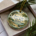 A decorative ornament in a box, featuring a scenic image of Burt Lake State Park in Michigan.