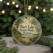 A circular ornament with a scenic image of a lake and trees, surrounded by Christmas lights, placed on a surface with pine branches.
