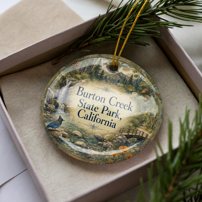 A decorative ornament in a box, featuring a scenic landscape with a bird, a bridge, and trees, along with the text "Burton Creek State Park, California".