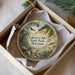 A round ornament with a scenic landscape of cliffs, trees, and a river, hanging from a string.