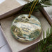 A decorative ornament in a box, featuring a scenic image of Camp Helen State Park, Florida.