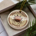 A decorative ornament in a box, featuring a spiny spider image and the text "SPINNY OR WEAVER SPIDER".