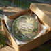 A decorative ornament in a wooden box, featuring a scenic landscape with a river and a cabin, with the text "Carr Creek State Park, Kentucky" printed on it.
