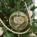 A round ornament hanging on a Christmas tree, featuring a scenic landscape with a castle and a river.