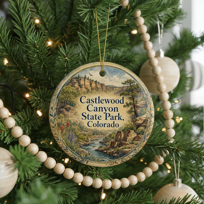 A round ornament hanging on a Christmas tree, featuring a scenic image of Castlewood Canyon State Park, Colorado.