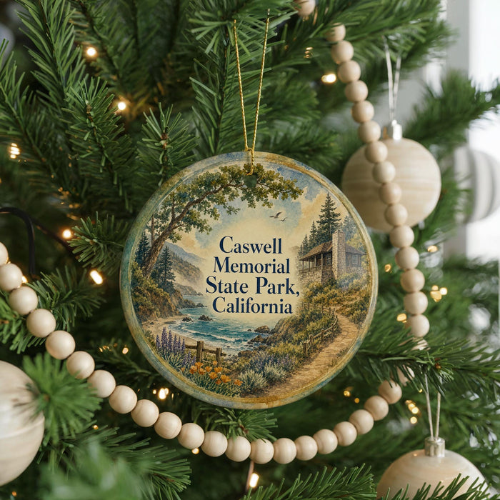 A round ornament hanging on a Christmas tree, featuring a scenic landscape with a river, mountains, and a cabin.